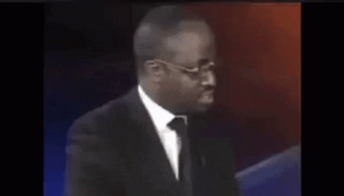 A Man In A Suit And Tie Is Sitting In Front Of A Red And Blue Background . GIF