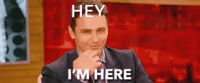 A Man In A Suit And Tie Is Sitting In Front Of A Red Background And Making A Funny Face . GIF