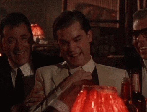 A Man In A Suit And Tie Is Sitting In Front Of A Red Lamp GIF