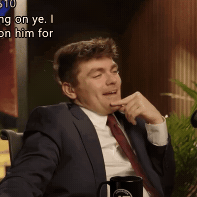 A Man In A Suit And Tie Is Sitting In Front Of A Sign That Says ' $ 10 ' On It GIF