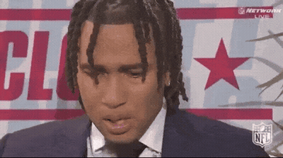 A Man In A Suit And Tie Is Sitting In Front Of A Sign That Says Nfl GIF