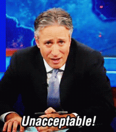 A Man In A Suit And Tie Is Sitting In Front Of A Sign That Says Unacceptable GIF