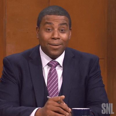 A Man In A Suit And Tie Is Sitting In Front Of A Snl Logo GIF