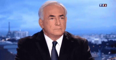 A Man In A Suit And Tie Is Sitting In Front Of A TV Screen That Says Tfi GIF