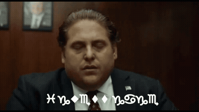 A Man In A Suit And Tie Is Sitting In Front Of A Wall With A Sign That Says Hnm On It GIF