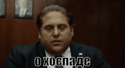 A Man In A Suit And Tie Is Sitting In Front Of A Wall With His Eyes Closed And Making A Funny Face . GIF