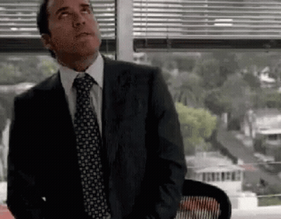 A Man In A Suit And Tie Is Sitting In Front Of A Window And Looking Up . GIF