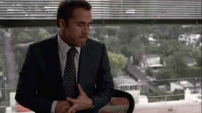 A Man In A Suit And Tie Is Sitting In Front Of A Window In An Office . GIF