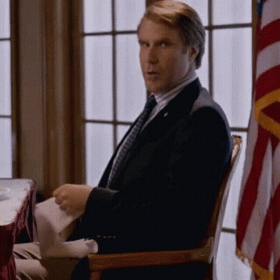 A Man In A Suit And Tie Is Sitting In Front Of A Window GIF