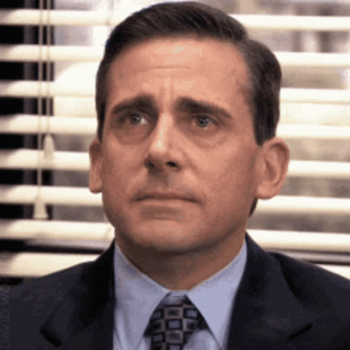 A Man In A Suit And Tie Is Sitting In Front Of A Window GIF