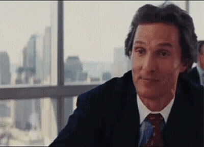 A Man In A Suit And Tie Is Sitting In Front Of A Window Looking Out . GIF