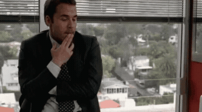 A Man In A Suit And Tie Is Sitting In Front Of A Window With His Hand On His Chin . GIF