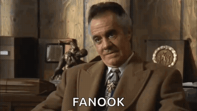 A Man In A Suit And Tie Is Sitting In Front Of A Wooden Wall And Talking . GIF
