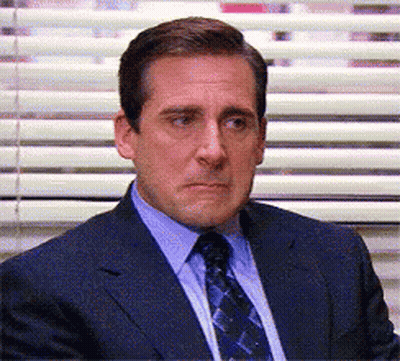 A Man In A Suit And Tie Is Sitting In Front Of Blinds GIF
