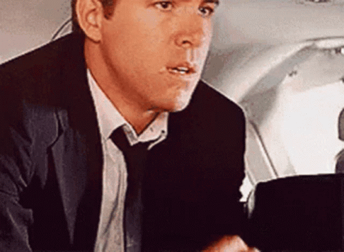 A Man In A Suit And Tie Is Sitting In The Back Seat Of A Plane . GIF