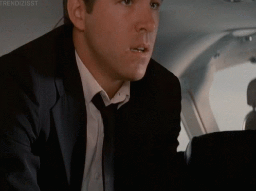 A Man In A Suit And Tie Is Sitting In The Back Seat Of A Plane GIF