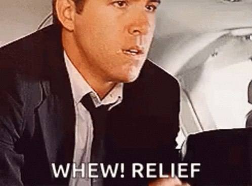 A Man In A Suit And Tie Is Sitting In The Back Seat Of An Airplane And Says `` Whew ! Relief '' . GIF
