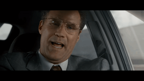 A Man In A Suit And Tie Is Sitting In The Driver 'S Seat Of A Car GIF