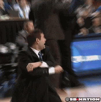 A Man In A Suit And Tie Is Sitting In The Stands Watching A Basketball Game . GIF