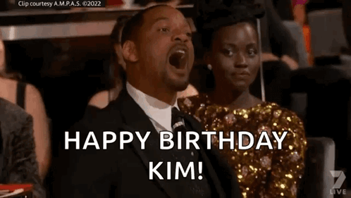 A Man In A Suit And Tie Is Sitting Next To A Woman In A Dress And Says `` Happy Birthday Kim '' . GIF
