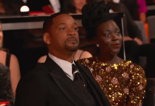 A Man In A Suit And Tie Is Sitting Next To A Woman In A Gold Dress GIF