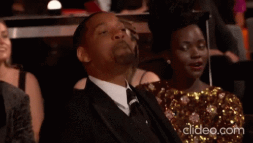 A Man In A Suit And Tie Is Sitting Next To A Woman In A Gold Dress GIF