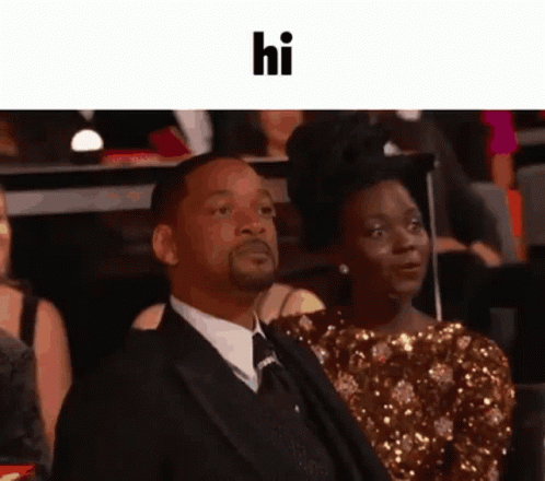 A Man In A Suit And Tie Is Sitting Next To A Woman In A Gold Dress And Says Hi GIF
