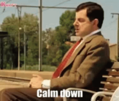 A Man In A Suit And Tie Is Sitting On A Bench With The Words Calm Down Written On It . GIF