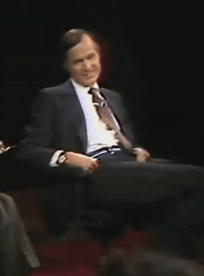 A Man In A Suit And Tie Is Sitting On A Chair GIF