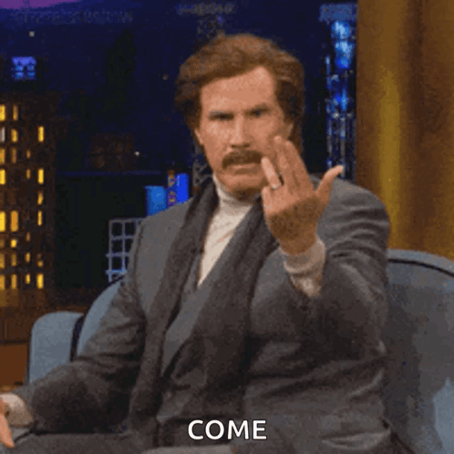 A Man In A Suit And Tie Is Sitting On A Couch And Giving The Middle Finger And The Word Come Is Visible GIF