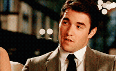 A Man In A Suit And Tie Is Sitting On A Couch Talking To Another Man . GIF