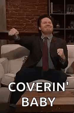 A Man In A Suit And Tie Is Sitting On A Couch With His Arms In The Air . GIF