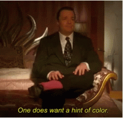 A Man In A Suit And Tie Is Sitting On A Couch With The Words One Does Want A Hint Of Color Below Him GIF