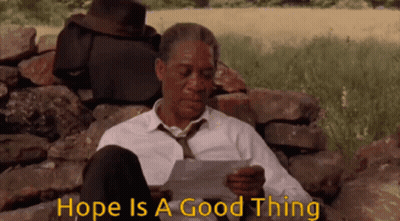 A Man In A Suit And Tie Is Sitting On A Rock Reading A Piece Of Paper . GIF