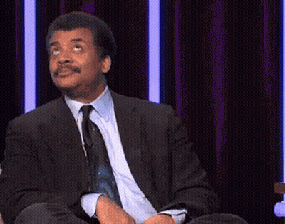 A Man In A Suit And Tie Is Sitting On A Stage With The Words `` Just Kidding '' Written On The Screen . GIF
