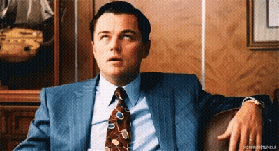 A Man In A Suit And Tie Is Sitting With His Hand On His Knee GIF