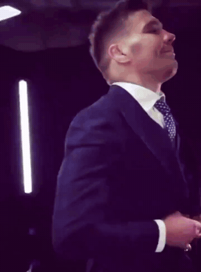 A Man In A Suit And Tie Is Smiling And Adjusting His Jacket GIF