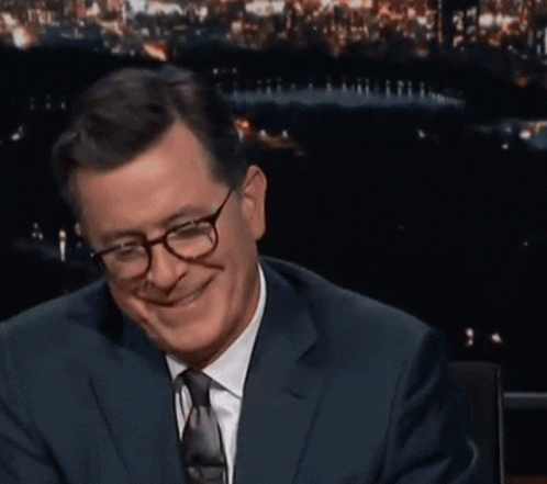 A Man In A Suit And Tie Is Smiling And Holding Something In His Hand GIF