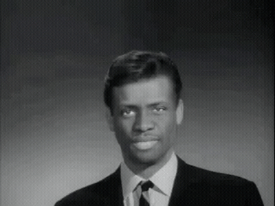 A Man In A Suit And Tie Is Smiling And Looking At The Camera . GIF
