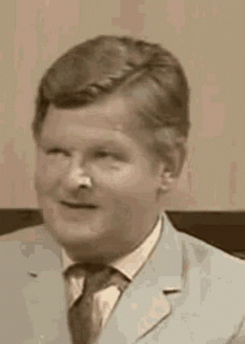 A Man In A Suit And Tie Is Smiling And Looking At The Camera In A Black And White Photo . GIF