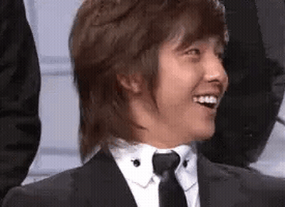 A Man In A Suit And Tie Is Smiling And Looking At The Camera . GIF