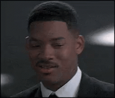 A Man In A Suit And Tie Is Smiling And Looking At The Camera . GIF
