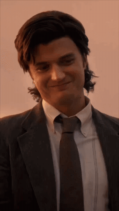 A Man In A Suit And Tie Is Smiling And Looking At The Camera . GIF