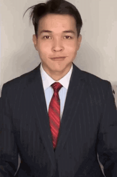 A Man In A Suit And Tie Is Smiling And Looking At The Camera . GIF