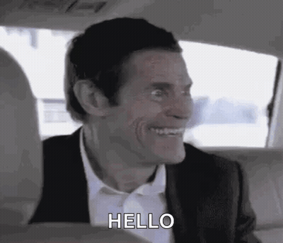 A Man In A Suit And Tie Is Smiling And Saying Hello While Sitting In The Back Seat Of A Car . GIF