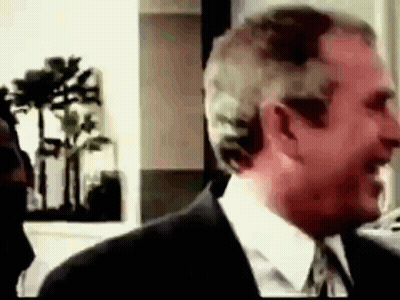 A Man In A Suit And Tie Is Smiling And Talking To Another Man . GIF