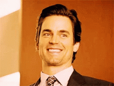 A Man In A Suit And Tie Is Smiling For The Camera GIF
