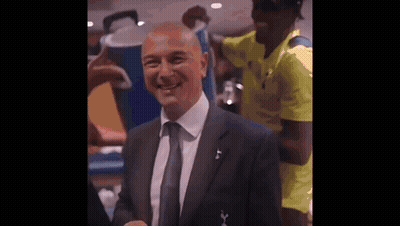 A Man In A Suit And Tie Is Smiling For The Camera While A Man In A Yellow Shirt Stands Behind Him . GIF