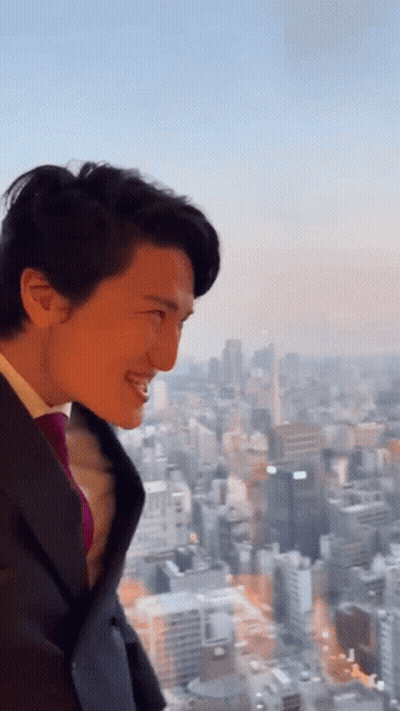 A Man In A Suit And Tie Is Smiling In Front Of A City Skyline GIF