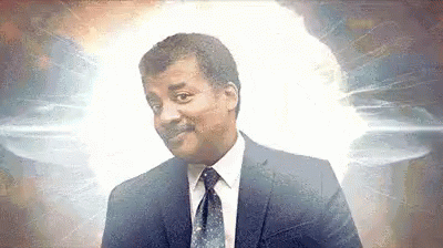 A Man In A Suit And Tie Is Smiling In Front Of A Glowing Light . GIF
